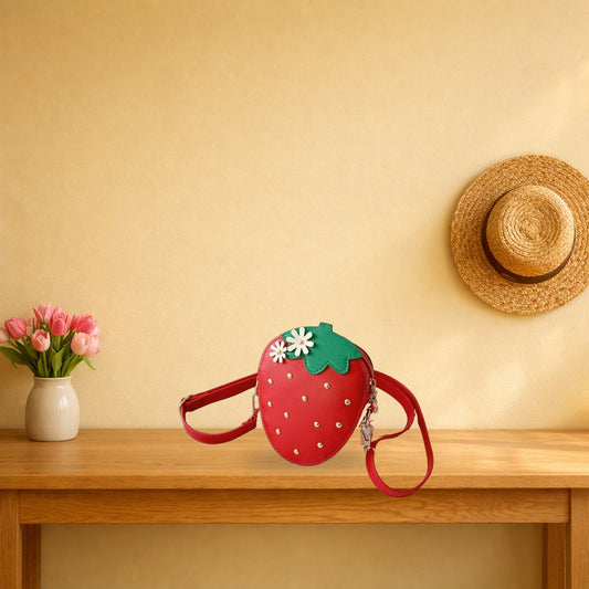 Red strawberry crossbody bag on a light oak console table