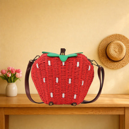 Woven strawberry crossbody bag with its brown strap on an oak hall table