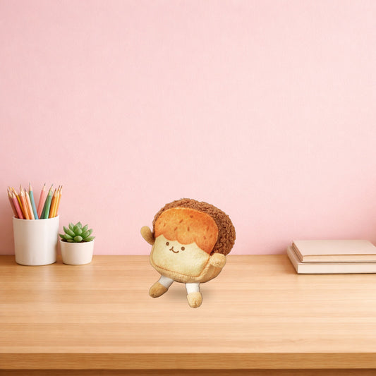 Golden toast plush keychain sitting on a light oak desk