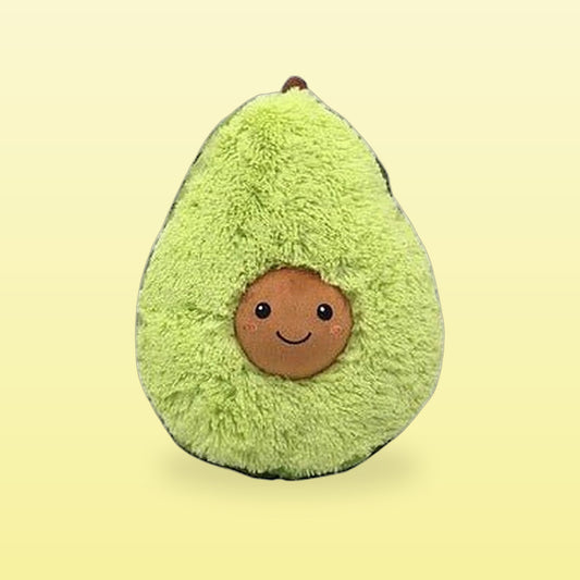 Fluffy green avocado plush hug pillow with a smiling pit face, on a butter yellow background