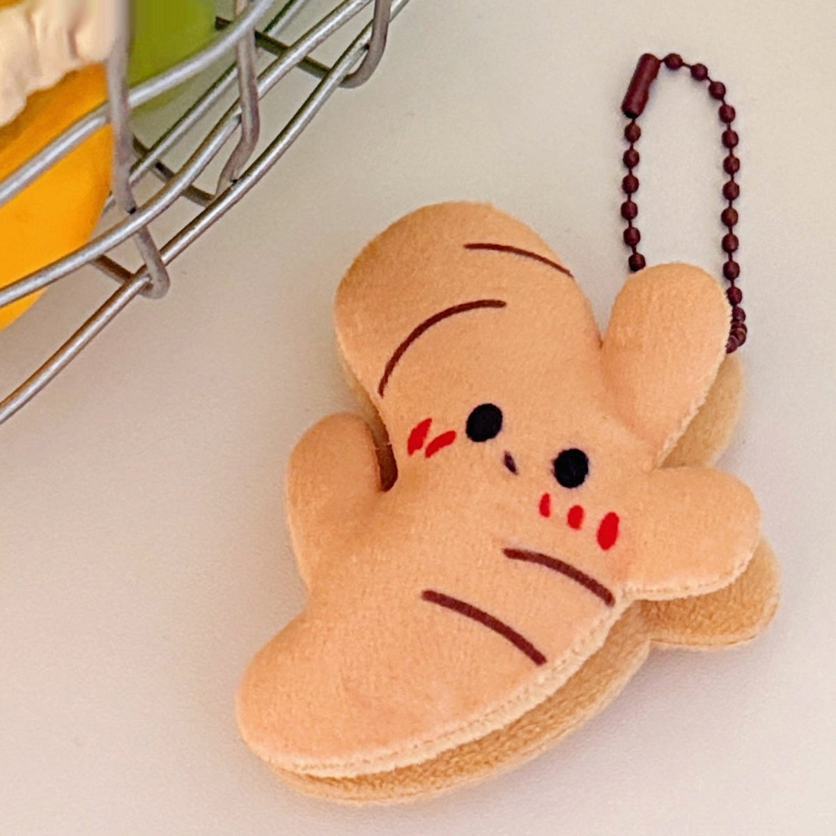 One tan plush ginger-shaped keychain with black eyes, red cheek marks, brown stripes and a brown chain.