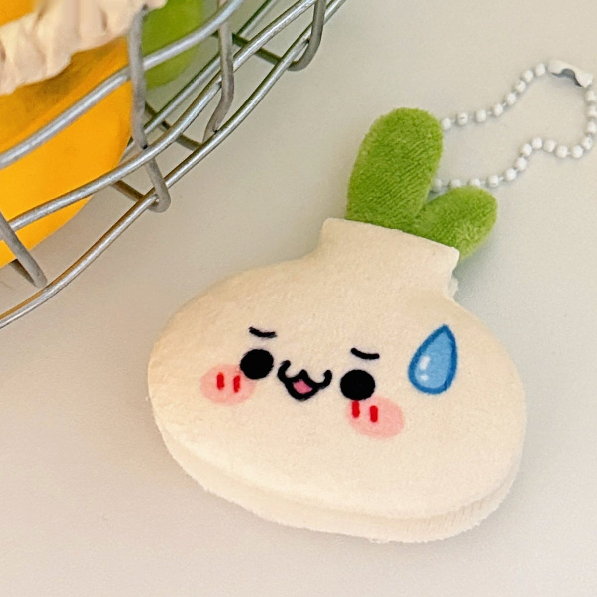 One cream plush onion keychain with green leaves, ball chain, black eyes, pink blush and blue sweat drop.